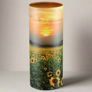 Peut inclure: Une urne funéraire cylindrique avec un coucher de soleil et un champ de tournesols imprimés sur le côté.