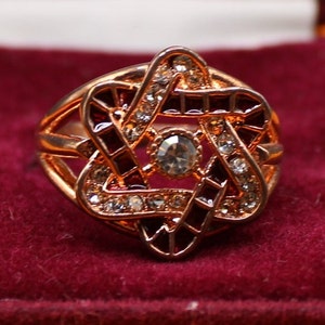 May include: A gold-tone ring featuring a red and white Star of David design. The ring is set with clear rhinestones.