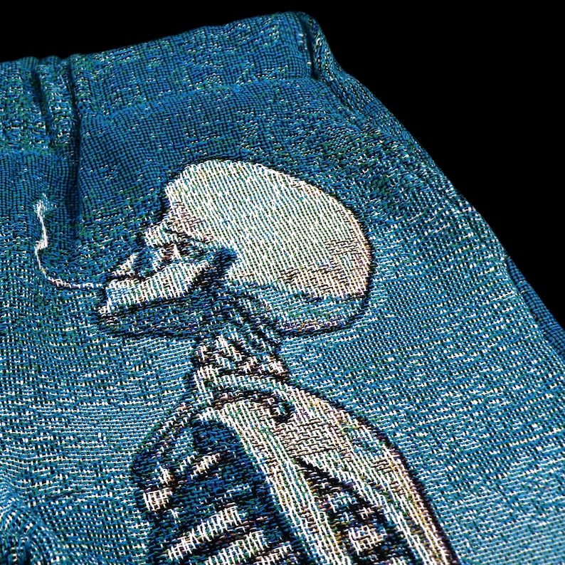 May include: A blue tapestry with a white skeleton design. The skeleton is depicted in a standing pose with its arms raised.