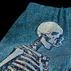 May include: A blue tapestry featuring a skeleton with a cigarette in its mouth. The skeleton is woven into the fabric and has a detailed design.