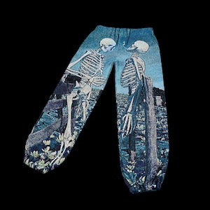 May include: Blue sweatpants with a tapestry-like design featuring two skeletons smoking cigarettes. The skeletons are standing in a field with a fence and flowers.