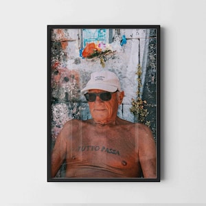 May include: A framed photographic print featuring a shirtless person wearing a light-colored baseball cap with the text NOT FROM PARIS MADAME and dark sunglasses. The person has a tattoo on their chest that reads TUTTO PASSA.