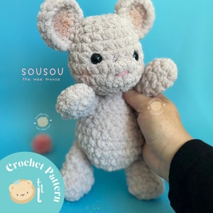 May include: A crocheted plush mouse toy in a light pink color with black eyes and a pink nose. The toy is being held by a hand against a light blue background. The text "Sousou the wee mouse" is visible in the top left corner of the image. The text "Crochet Pattern" is visible in the bottom left corner of the image.