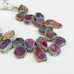 May include: A strand of faceted ruby beads with a mix of blue, green, and red hues. The beads are irregular in shape and have a rough, natural finish.