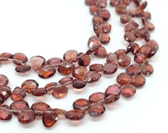 May include: A strand of faceted, reddish-brown gemstone beads. The beads are oval-shaped and have a smooth, polished finish.