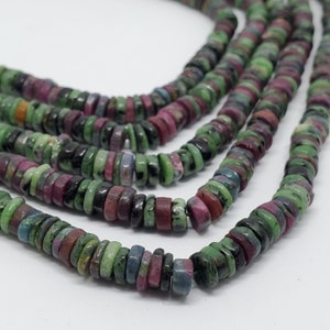 May include: Strands of gemstone beads. The beads are flat, circular, and feature a mix of colors including green, red, and black. The beads are strung together, creating a layered effect. The gemstones appear to be natural, with variations in color and texture.