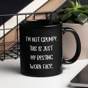 May include: Black coffee mug with white text that reads "I'm not grumpy. This is just my resting work face."