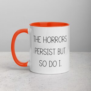 May include: White ceramic mug with an orange rim. The mug has black text that reads "The Horrors Persist But So Do I."