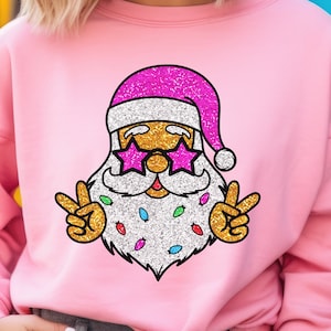 May include: Pink sweatshirt with a glitter design of Santa Claus wearing sunglasses and peace signs. The design is in pink, gold, white, and multi-colored glitter.