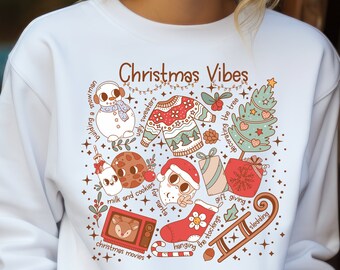 Puede incluir: Sudadera blanca con un diseño navideño que presenta ilustraciones de un muñeco de nieve, un árbol de Navidad, una media, un regalo, una galleta, un vaso de leche, un suéter navideño, una chimenea y un bastón de caramelo. El texto "Christmas Vibes" está escrito en marrón en la parte superior del diseño. El texto alrededor de las ilustraciones incluye "building a snowman", "ugly sweaters", "milk and cookies", "for santa", "decorating the tree", "gift giving", "hanging the stockings", "christmas movies", y "sledding".