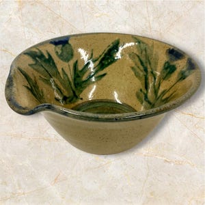May include: A brown ceramic bowl with a green and blue floral design. The bowl has a slightly uneven rim and a pouring spout.