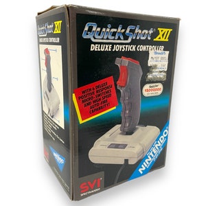 May include: A vintage QuickShot XII Deluxe Joystick Controller box. The box is black with blue and red accents, featuring the Nintendo logo. The joystick is gray with a red button. Text on the box includes "QuickShot XII" and "Deluxe Joystick Controller."
