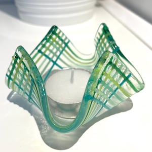Può includere: Un portacandele in vetro verde acqua e verde con un motivo geometrico. Il portacandele è progettato per contenere una piccola candela tealight.