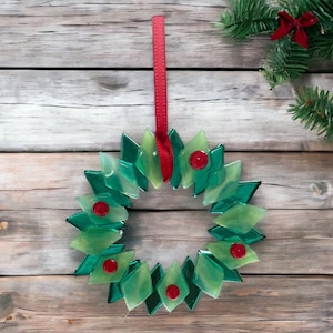 May include: A green glass Christmas wreath with red bows hanging on a wooden background.
