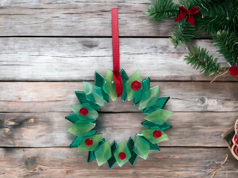 May include: A green glass Christmas wreath with red bows hanging on a wooden background.