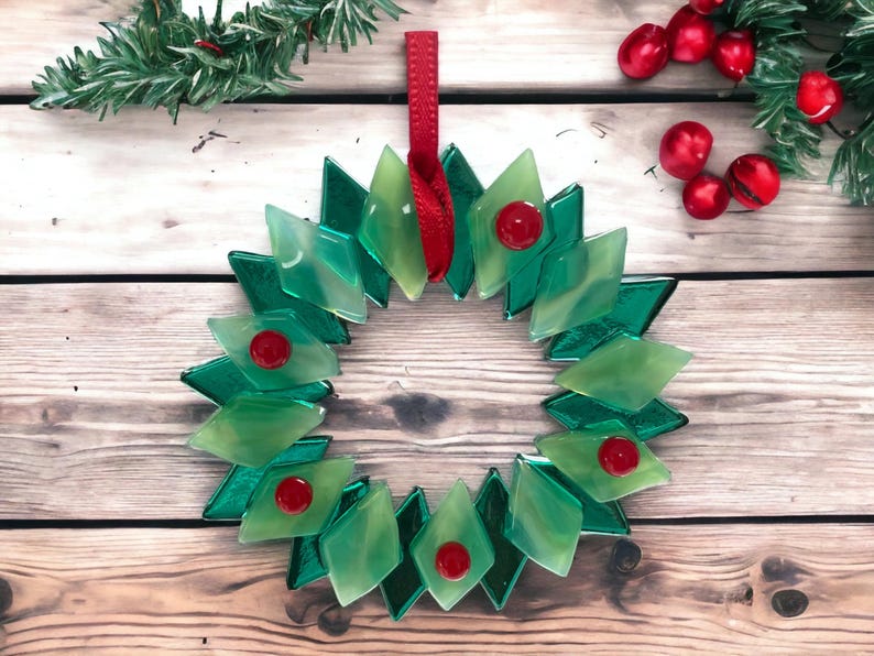 May include: A green glass Christmas wreath with red berries. The wreath is made of individual diamond-shaped pieces of glass.