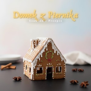 May include: A gingerbread house with white icing accents, a wreath, and decorative details. The house has a chimney and windows. The image also includes star anise and cinnamon sticks.