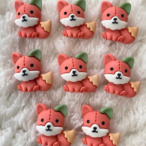 Puede incluir: Colección de siete pequeños adornos con forma de zorro naranja. Cada zorro tiene una cara blanca, orejas verdes y una cola de color canela. Los zorros están sentados, con ojos negros y un diseño cosido.