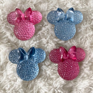 May include: Four sparkly Minnie Mouse head-shaped embellishments. Two are pink with a pink bow and two are blue with a blue bow.