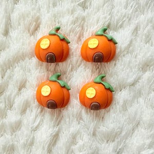 Könnte beinhalten: Vier orangefarbene Kürbis-Dekorationen mit grünen Stielen und braunen Türen. Jeder Kürbis hat ein gelbes kreuzförmiges Fenster. Die Kürbisse sind auf einer weißen, flauschigen Oberfläche angeordnet, ideal für Halloween oder Herbstbasteln.