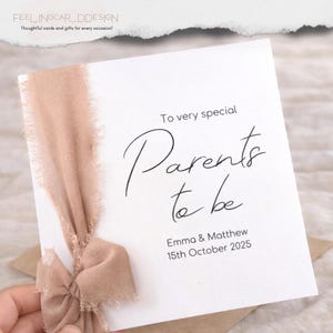May include: A square white greeting card featuring the black printed text To very special Parents to be, Emma & Matthew, 15th October 2025. The card is decorated with a dusty rose coloured frayed chiffon ribbon tied in a bow on the left side.