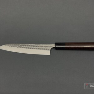 May include: A Japanese-style kitchen knife with a hammered blade and a dark wooden handle. The blade is silver and the handle is a dark brown color. The knife is designed for precision cutting and is ideal for culinary tasks.