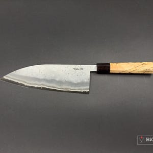 May include: A Japanese-style chef's knife with a wooden handle and a black bolster. The blade is made of steel and has a hammered finish.