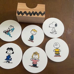 Posavasos con personajes de dibujos animados extravagantes que presentan un amado beagle y sus amigos. Diámetro de 4", 6 posavasos con soporte.