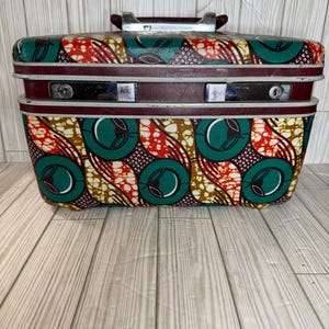 May include: A vintage, hard-sided, two-tone suitcase with a burgundy and white exterior. The suitcase has a green, orange, and yellow patterned design with a repeating circle motif.