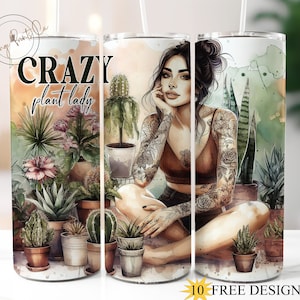 Puede incluir: Un vaso blanco con un diseño de acuarela que presenta a una mujer con tatuajes y plantas. El texto "Crazy plant lady" está impreso en el vaso.