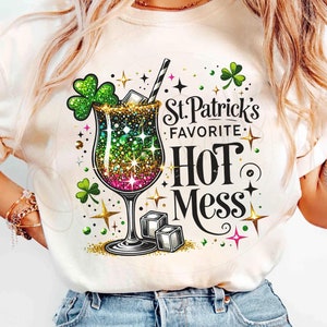 Pode incluir: Camiseta branca com um trevo verde, um copo de coquetel brilhante e o texto "St. Patrick's Favorite Hot Mess".