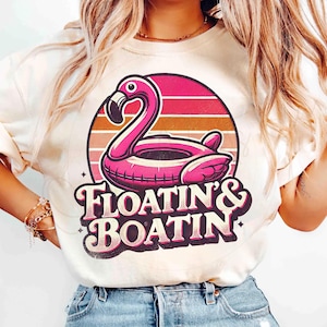 May include: White t-shirt with a pink flamingo pool float graphic and the text "Floatin' & Boatin'" in a retro font.