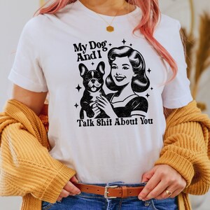 Może przedstawiać: Biała koszulka z czarno-białym obrazkiem kobiety trzymającej buldoga francuskiego. Tekst na koszulce brzmi "My Dog And I Talk Shit About You."