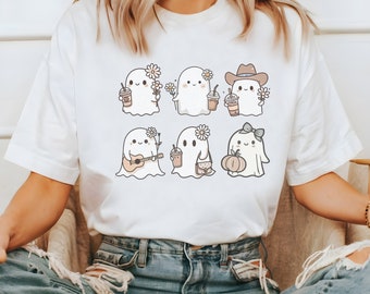 May include: White t-shirt with a graphic of six cute ghosts wearing different accessories, including a cowboy hat, a guitar, a pumpkin, and a purse. The ghosts are all wearing flowers in their hair.