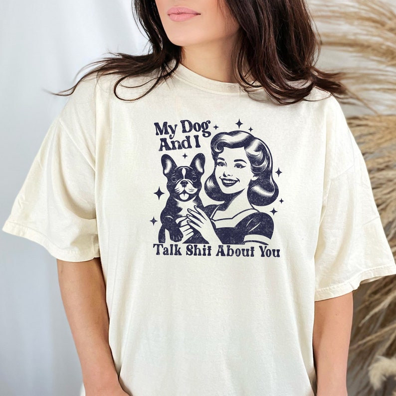 Może przedstawiać: Biały t-shirt z grafiką w stylu retro przedstawiającą kobietę trzymającą psa. Tekst na koszulce brzmi "My Dog And I Talk Shit About You."