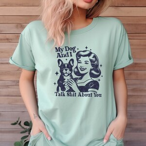 Może przedstawiać: Jasnozielony t-shirt z grafiką w stylu vintage przedstawiającą kobietę trzymającą buldoga francuskiego. Tekst na koszulce brzmi "My Dog And I Talk Shit About You."