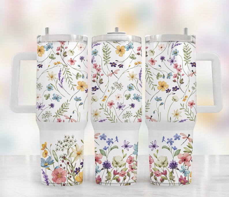 May include: Three stainless steel tumblers with a white background and a floral pattern in shades of pink, yellow, blue, and green. The tumblers have a handle and a lid.