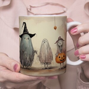 May include: A white ceramic mug with a Halloween-themed design. Three ghosts are depicted, one wearing a witch's hat, another holding a stick, and the third carrying a jack-o'-lantern. The background is a light brown with a vintage look.