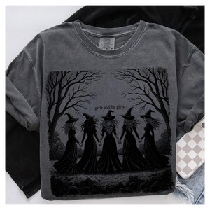 May include: Dark gray sweatshirt featuring a graphic of five witches holding hands under bare trees, with the text "girls will be girls." The design is in black, set against a faded gray background.