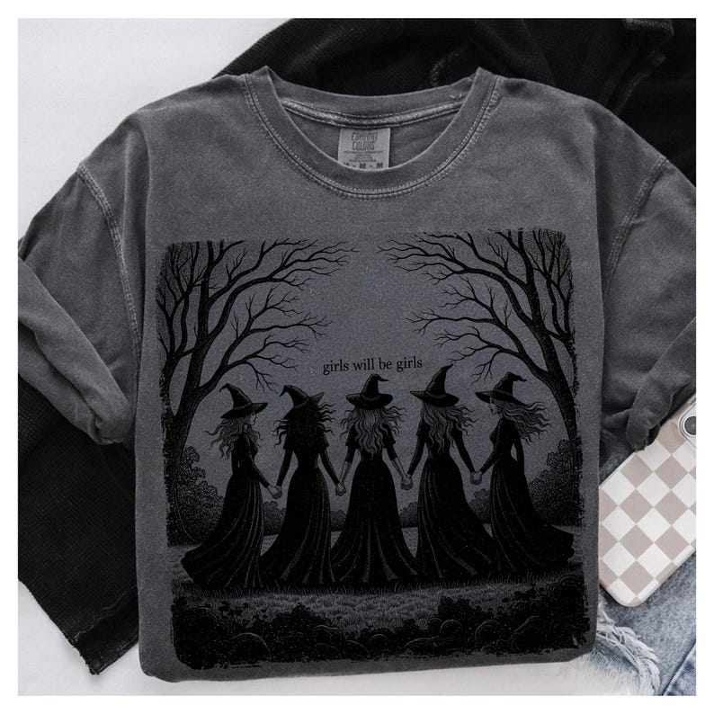 May include: Dark gray sweatshirt featuring a graphic of five witches holding hands under bare trees, with the text "girls will be girls." The design is in black, set against a faded gray background.