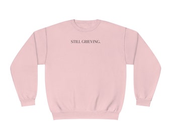 Puede incluir: Una sudadera rosa con el texto "STILL GRIEVING." impreso en la parte delantera.