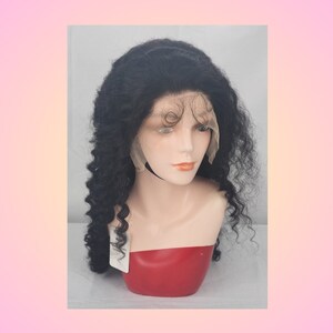 May include: A black curly human hair wig on a mannequin head. The wig is styled in a long, loose curl pattern. The wig is on a red mannequin head with a white base.