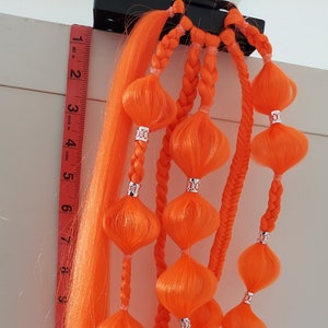 Può includere: Un set di extension per capelli arancioni con ciocche intrecciate e più pompon arancioni. Le extension sono lunghe circa 61 cm.