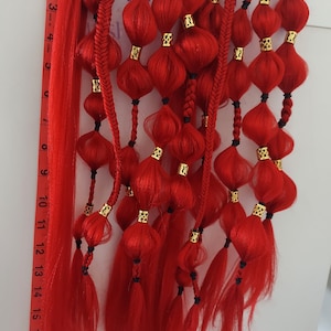 Può includere: Un set di extensioni per capelli rossi con perline dorate e dettagli in corda nera. Le extensioni sono intrecciate e legate insieme con un elastico nero. Le extensioni sono lunghe circa 50 cm.