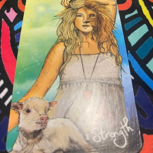 May include: A tarot card with a woman with a lion's head and a lamb at her feet. The card is titled "Strength".
