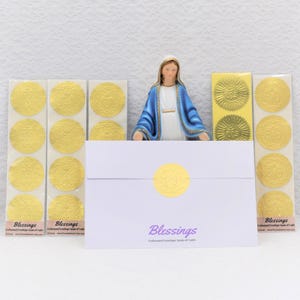 May include: A religious-themed display featuring a statue of the Virgin Mary, gold-colored embossed envelope seals, and a white envelope with the word "Blessings" printed on it. The seals and envelope have a matching design.