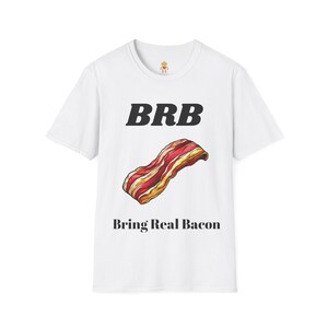 Könnte beinhalten: Weißes T-Shirt mit dem Text "BRB" über einer farbenfrohen Abbildung von Speck. Unter dem Speckbild steht der Text "Bring Real Bacon". Es handelt sich um ein Freizeitkleidungsstück.