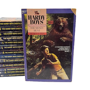 Puede incluir: La portada del libro "Los Hardy Boys #101: La Caza del Dinero" muestra a un joven corriendo de un gran oso marrón en un bosque. El texto de la portada dice "Los Hardy Boys 101 La Caza del Dinero" y "Una cabaña de caza encantada esconde un secreto asombroso..."