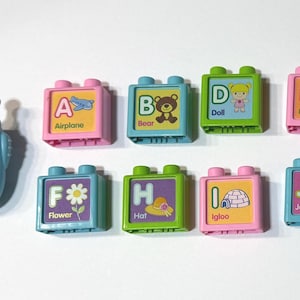 May include: A blue toy phone with a smiling face and a set of colorful alphabet blocks. Each block features a letter and a corresponding image, such as an airplane, bear, doll, egg, flower, hat, igloo, and jacket.