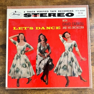 May include: A vintage record album cover featuring three women in white dresses with floral patterns, dancing against a red background. The album title is "Let's Dance" with the artist "David Carroll and His Orchestra".